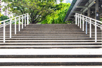 Building exterior stairs with brown granite tiles or concrete with handrails tree green is background. Structure of brick tile paved staircase amidst bright sunlight. People traveling up and down.