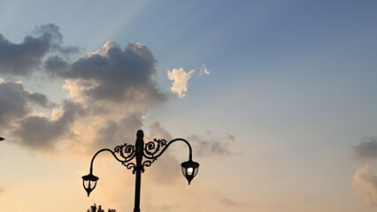 A silhouette of an ornate vintage lamppost against a beautiful sunset sky with clouds and sun rays.