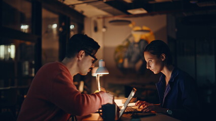 Successful coworkers enjoying win looking laptops at night office closeup. 