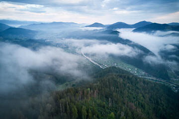 Breathtaking aerial view of valley enveloped in morning mist, with river winding through lush green hills and village nestled among trees.