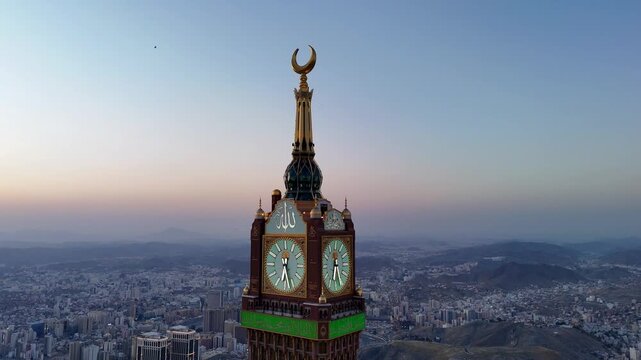 drone footage of Mecca, Saudi Arabia, filmed at sunset. The video captures the vast urban landscape with residential buildings, modern towers, and surrounding mountains bathed in golden hour light