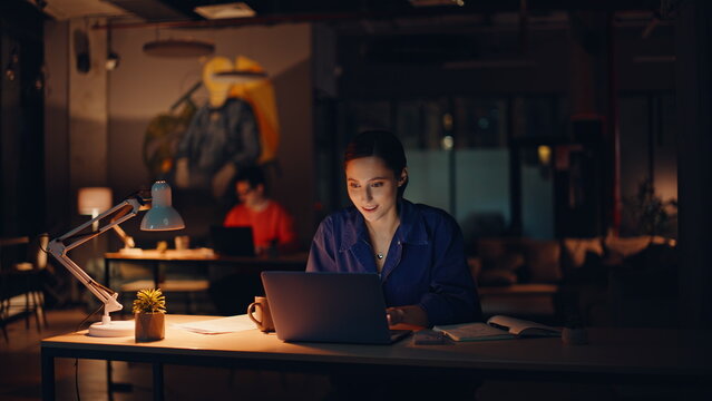 Teammates focused deadline job in night office. Smiling woman looking laptop
