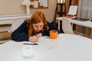 A teenage girl studies in the living room during evening hours, drinking coffee while focusing on...