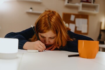 A teenage girl studies in the living room during evening hours, drinking coffee while focusing on...