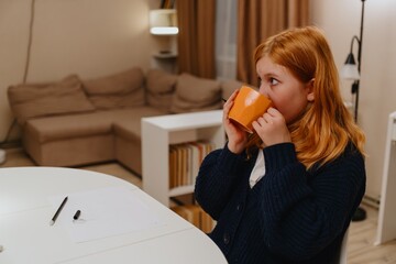 A teenage girl studies in the living room during evening hours, drinking coffee while focusing on...