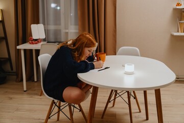 A teenage girl studies in the living room during evening hours, drinking coffee while focusing on...