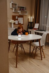A teenage girl studies in the living room during evening hours, drinking coffee while focusing on homework. Captures authentic student life and modern study routines