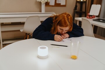 A teenage girl studies in the living room during evening hours, drinking coffee while focusing on...