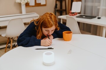 A teenage girl studies in the living room during evening hours, drinking coffee while focusing on...