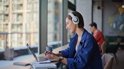Headphones hipster typing laptop in urban cafeteria closeup. Smiling woman 