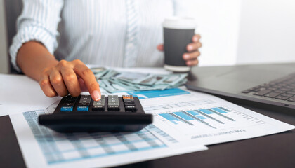 A businesswoman in a striped shirt is calculating finances with a calculator.