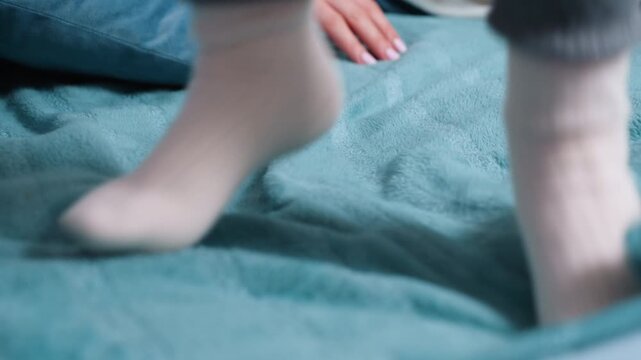 Child feet in warm socks jumping on soft bed blanket, creating cozy playful atmosphere of childhood comfort, relaxation, and carefree indoor lifestyle with focus on details of home warmth