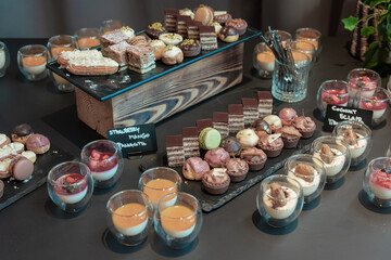 dessert buffet table filled with assorted sweets, including layered chocolate cakes, colorful macarons, mini tarts, cream puffs, and elegant glass cups of mousse, panna cotta, and fruit desserts.