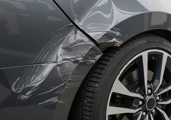 Close up of a damaged car fender with deep scratches and dents on the gray paint, depicting a common road accident scenario and need for repair service.