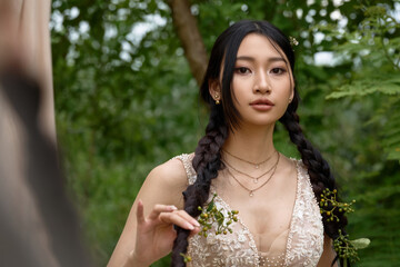 Girl in white dress standing near green trees.