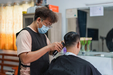 Hair stylist trims hair with clippers in a modern barbershop setting with warm lighting and floral decoration in the background