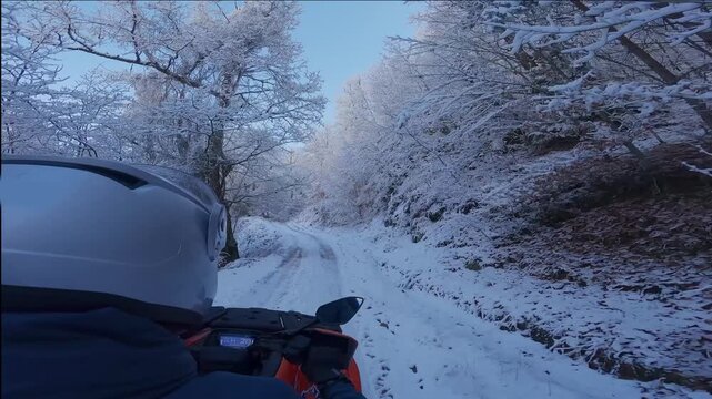 A man is riding a motorcycle on a snowy road. The man is wearing a helmet and a blue jacket. Concept of adventure and excitement as the man navigates the snowy terrain on his motorcycle