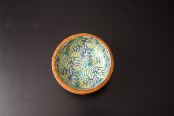 A round wooden bowl with hand-painted leaves on the inside that looks a bit like a jungle