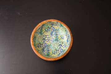A round wooden bowl with hand-painted leaves on the inside that looks a bit like a jungle