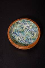 A round wooden bowl with hand-painted leaves on the inside that looks a bit like a jungle