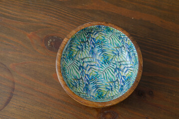 A round wooden bowl with hand-painted leaves on the inside that looks a bit like a jungle