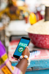 Mobile payment confirmed on a smartphone held by Local African market woman at her outdoor stall. Small business owner, SME.