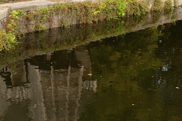 Distorted reflection of a stone building with plants on the water surface.