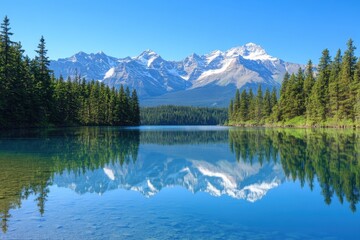 Fototapeta premium Sharp crisp image of crystal clear lake reflecting snow capped mountain peaks and green pine trees under bright blue sky on calm day