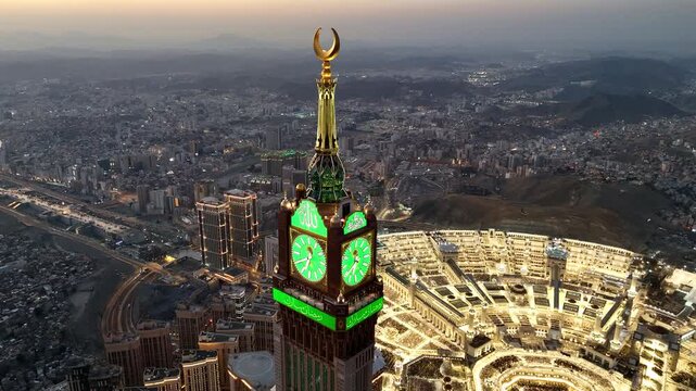 drone footage of Mecca, Saudi Arabia, filmed at sunset. The video captures the vast urban landscape with residential buildings, modern towers, and surrounding mountains bathed in golden hour light