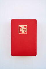 Close-up of a bright red fire hose cabinet mounted on a white wall. The golden symbol indicates essential safety equipment for emergency response.