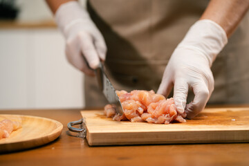 hands cutting chicken on a wooden cutting board in the kitchen, preparing to cook.