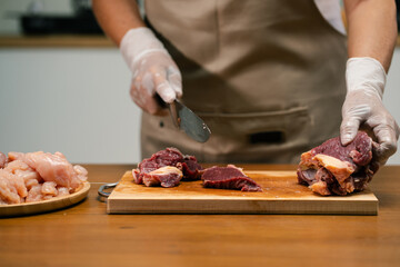 Asian man's hands cutting meat on a wooden cutting board in the kitchen, preparing to cook.