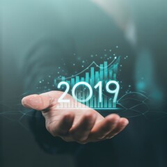 Obraz premium Vision of 2019: A person's hand tenderly cradles a glowing, futuristic digital representation of financial growth and data analysis. The year 2019 is prominently displayed, symbolizing progress.