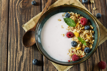 A delicious and nutritious breakfast bowl featuring creamy yogurt, crunchy granola, and a delightful mix of fresh berries, all arranged beautifully on a rustic wooden table