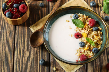 Healthy breakfast bowl with yogurt, granola, and fresh berries served on a wooden table in a cozy kitchen setting