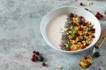 Healthy breakfast bowl featuring yogurt, fresh berries, chia seeds, and granola in a stylish setting on a gray surface