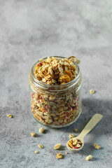 Healthy breakfast granola in a glass jar on a gray countertop with a wooden spoon beside it at morning time