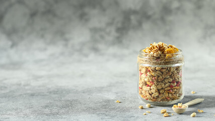 Crunchy granola in a glass jar sits on a stone surface, showcasing a healthy breakfast option with oat clusters and dried fruits