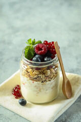 Colorful fruit and granola parfait in a jar displayed on a textured surface with a wooden spoon and napkin