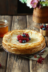 Delicious crepes are artfully stacked high, generously adorned with an array of fresh berries and a drizzle of honey, all enjoyed in a warm and inviting wooden environment