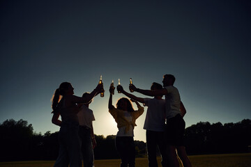 Black silhouettes. Dark photo of people cheering, celebrating, holding beer bottles