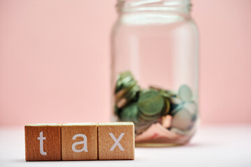 savings jar and toy block  with text tax against pink background.