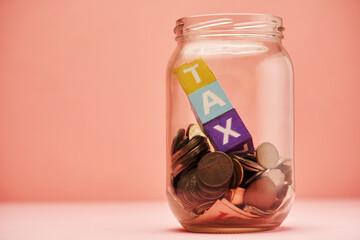 savings jar and toy block  with text tax against pink background.