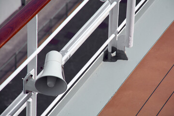 Close up of a passenger safety megaphone mounted on a white cruise ship railing. The equipment is crucial for announcing alerts and important messages.