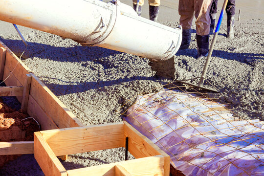 Construction workers pour wet cement from chute into wooden formwork at building site cement is being poured over rebar grid that provides structural reinforcement for concrete foundation..