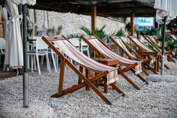 Outdoor relaxed space near a beach with wooden deck chairs with striped fabric arranged in a row...