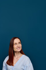 Fototapeta premium Woman with striking red hair smiling against a bold blue background