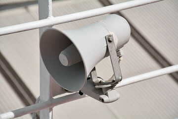 Close up of a passenger safety megaphone mounted on a white cruise ship railing. The equipment is crucial for announcing alerts and important messages.