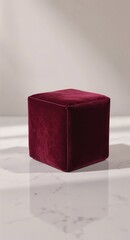 Minimalist scene with a single, elegant cube covered in rich, deep red velvet. It rests on a white marble surface with a soft window shadow. Perfect for a luxury product display or mockup