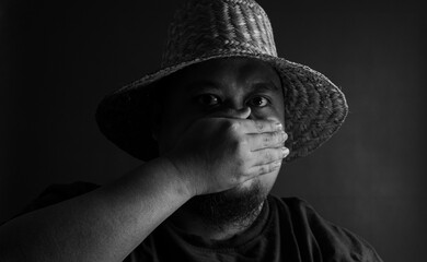 Man with straw hat covering mouth with hand, monochrome black and white portrait, symbol of...